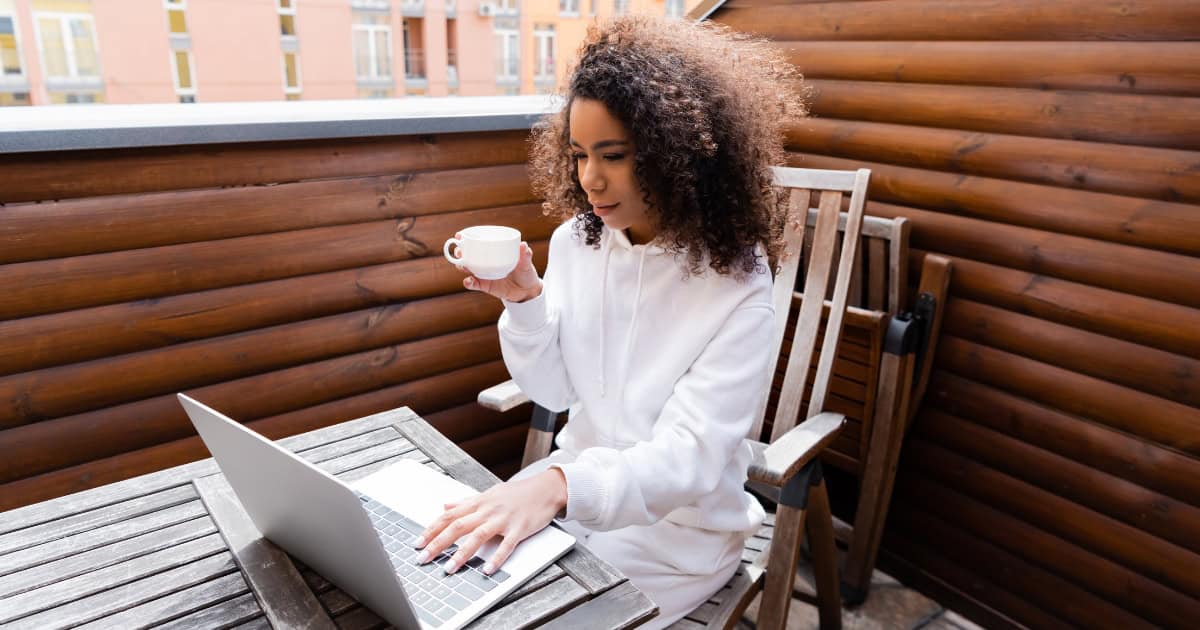 Woman drinking from a mug, working on a laptop