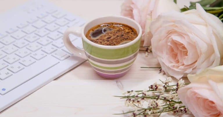 Desk with a keyboard, coffee, and flowers