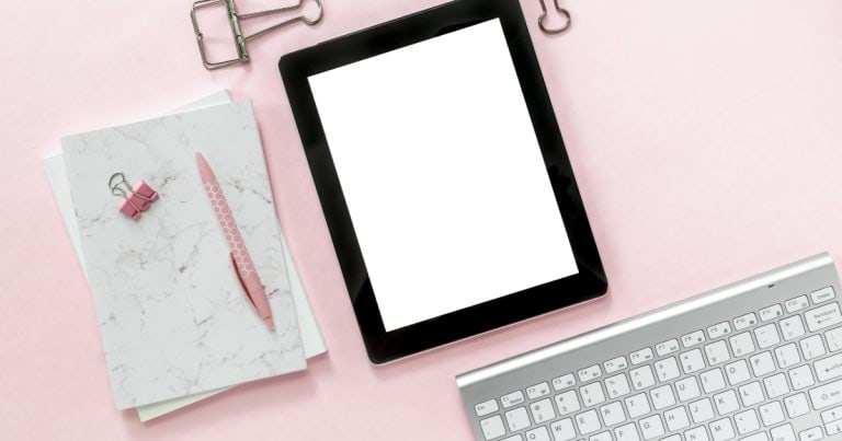 Desk with keyboard, tablet, notebook, pen, and paper clips