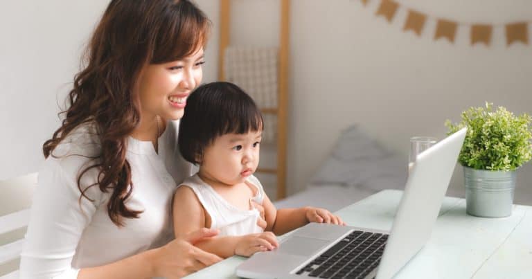 Woman holding her toddler while working on a laptop